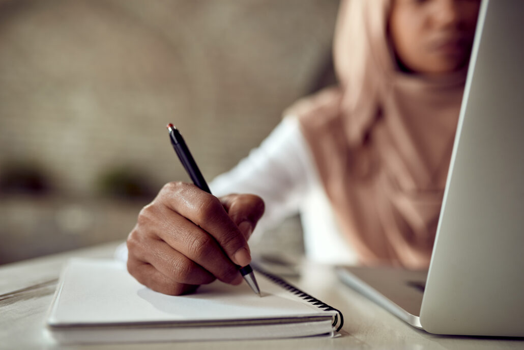 closeup black muslim businesswoman writing notes while working computer office